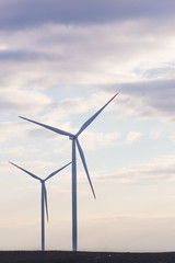 two wind turbines on agricultural ground with cloudy sky in background