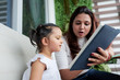 © DragonImages - Young mother holding book and teaching her little daughter to read while they sitting on sofa outdoors