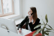© Westend61 - Young woman talking on cell phone at desk in office