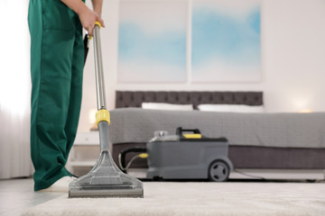 Canvas Print - Professional janitor removing dirt from carpet with vacuum cleaner in bedroom, closeup. Space for text