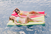Overhead View Of Brunette And Blonde Women Lying On Pool Floats In Swimming Pool