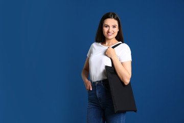 Wall Mural - Beautiful young woman with stylish blank eco bag against color background, space for text