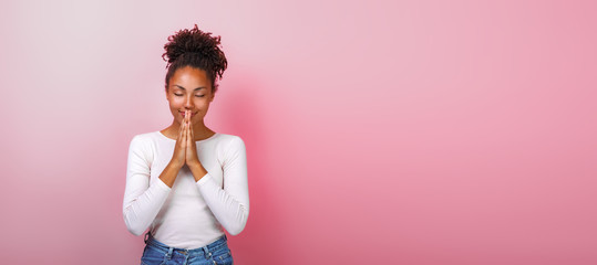 Wall Mural - Portrait of woman in supplication pose with smile and close eyes over pink background. Copyspace