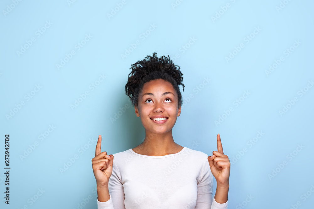 Attractive mulatto woman pointing by her both index fingers up to place for copy space - obrazy, fototapety, plakaty 
