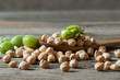 Uncooked dried chickpeas in wooden spoon with raw green chickpea pod plant on wooden table. Heap of legume chickpea background