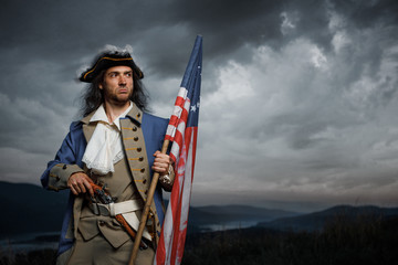 Soldier of United States War of Independence with flag and pistol posing over dramatic sky. 4th july History Concept photo