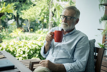 Senior Man Happiness Sitting And Holding Cup Of Coffee At Balcony Near Garden At Nursing Home For Relaxing