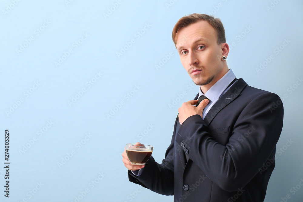 Handsome businessman with cup of coffee on light background