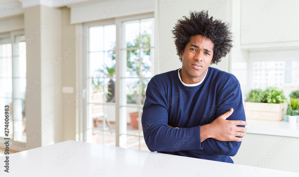Young african american man wearing casual sweater sitting at home shaking and freezing for winter cold with sad and shock expression on face