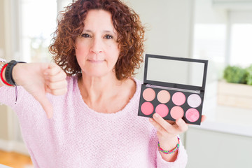 Wall Mural - Senior woman showing palette of pink blush with angry face, negative sign showing dislike with thumbs down, rejection concept