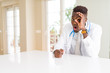 © Krakenimages.com - African american doctor man at the clinic doing ok gesture shocked with surprised face, eye looking through fingers. Unbelieving expression.