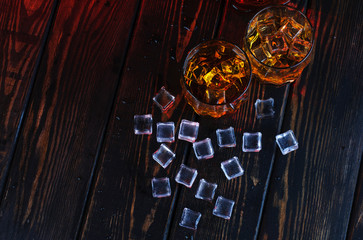 Wall Mural - Two glasses of whiskey with ice cubes served on wooden planks.