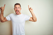 © Krakenimages.com - Young handsome man wearing casual white t-shirt over isolated background smiling amazed and surprised and pointing up with fingers and raised arms.