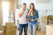 © Krakenimages.com - Young beautiful couple holding blackboard with new home text at new house cover mouth with hand shocked with shame for mistake, expression of fear, scared in silence, secret concept