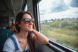 A young girl in sunglasses on the train looking out the window. Good mood in the journey