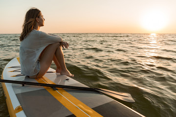 beautiful young woman sitting on a stand up paddle board