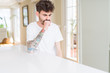 © Krakenimages.com - Young man wearing casual t-shirt sitting on white table feeling unwell and coughing as symptom for cold or bronchitis. Healthcare concept.