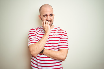 Wall Mural - Young bald man with beard wearing casual striped red t-shirt over white isolated background looking stressed and nervous with hands on mouth biting nails. Anxiety problem.