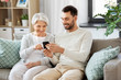 © Syda Productions - family, generation and people concept - happy smiling senior mother and adult son with smartphone networking at home