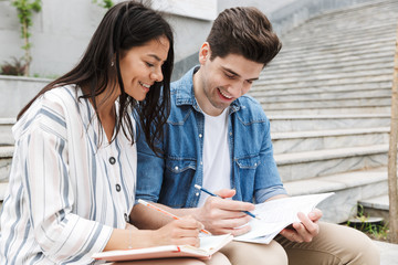 Canvas Print - Image of happy couple talking and studying while sitting on bench near stairs outdoors