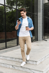 Poster - Happy young amazing man businessman posing outdoors outside walking chatting by mobile phone drinking coffee.