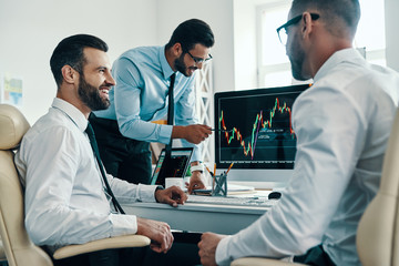 Market is growing. Group of young modern men in formalwear analyzing stock market data while working in the office