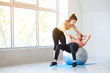 © Pixel-Shot - Young sporty woman with fitball doing exercises under supervision of her personal trainer in gym