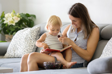 Sticker - Charming mother, showing images in a book to her cute toddler baby boy at home