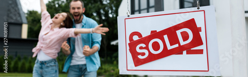Fotografía panoramic shot of board with sold lettering near happy man gesturing with woman