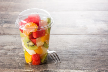 Fresh cut fruit in a plastic cup on wooden table. Copyspace