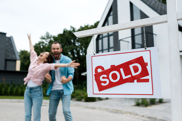 selective focus of board with sold lettering near happy man gesturing with woman