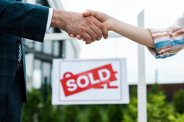 Wall Mural - selective focus of broker and woman shaking hands near board with sold letters