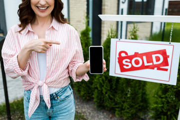 Wall Mural - cropped view of cheerful woman pointing with finger at smartphone with blank screen