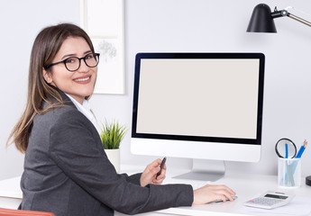 Young businesswoman wearing glasses sitting at her desk reading her blank white computer screen, profile view in the office