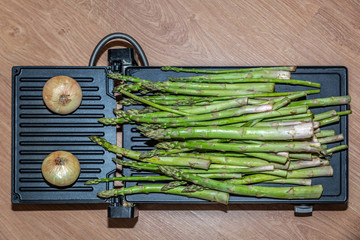 Green and tender asparagus and two onions on a grill placed on a wooden surface