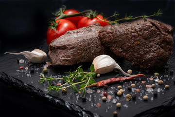 Wall Mural - Grass Fed Corn Roast Beef garnished with Tomatoes, Fresh Thyme, dried Red Chile Pepper, Garlic and Peppercorns on natural black stone background.