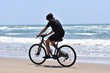 © Fotokalua - Cyclist riding in the edge of water on a deserted beach