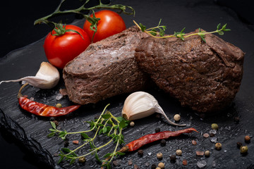 Wall Mural - Grass Fed Corn Roast Beef garnished with Tomatoes, Fresh Thyme, dried Red Chile Pepper, Garlic and Peppercorns on natural black stone background.