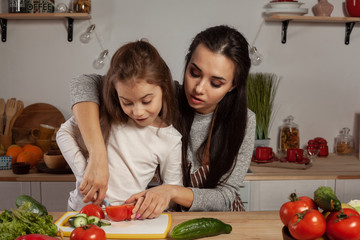 Mother and her daughter are making a vegetable salad and having fun at the kitchen.