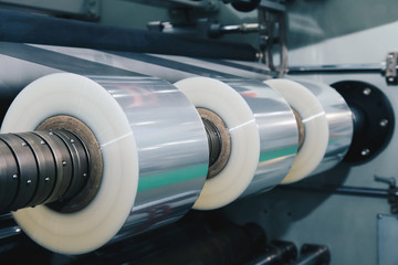 Wall Mural - roll of plastic packaging film on the automatic packing machine in food product factory. industrial and technology concept. vintage photo and film style.