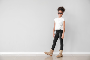 Wall Mural - Stylish African-American girl in jeans near light wall