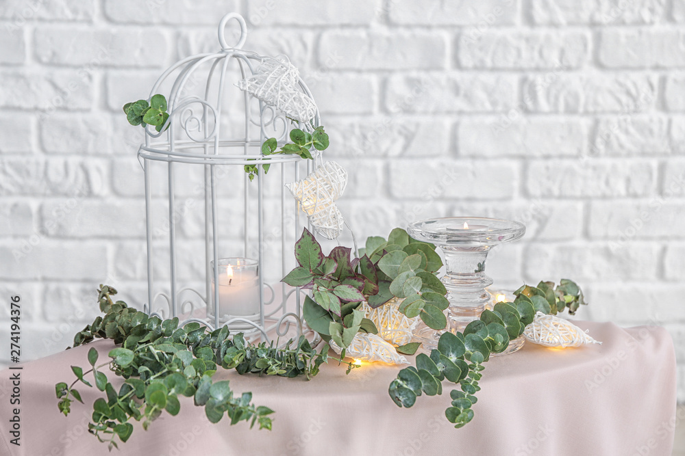 Decorative cage, burning candles and eucalyptus branches on table