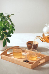 A hand pouring tea from glass teapot on wooden serving tray