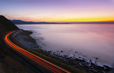 Wall Mural - car lights by the road by the sea at sunset