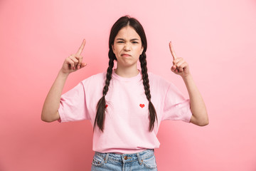 Sticker - Image of teen displeased girl with two braids looking at camera and pointing fingers upward at copyspace