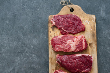 Poster - Raw black angus prime beef steak variety on vintage cutting board with rosemary, sea salt and spices