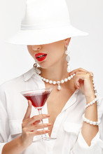 Beautiful Girl With A Glass Of Red Wine In Her Hand In An Elegant White Hat, Sunglasses And Exquisite Jewelry.