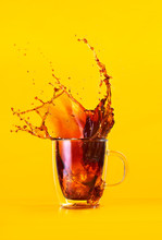 Glass Mug With Coffe Splashing In Front Of Orange Background