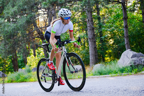 Fotomural Young Woman Cyclist Riding Road Bicycle on the Free Road in the Forest at Hot Summer Day