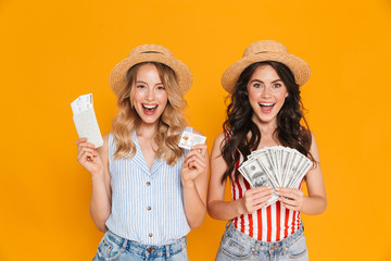 Wall Mural - Portrait of pretty women wearing straw hats holding credit card and money bills with passport and travel tickets